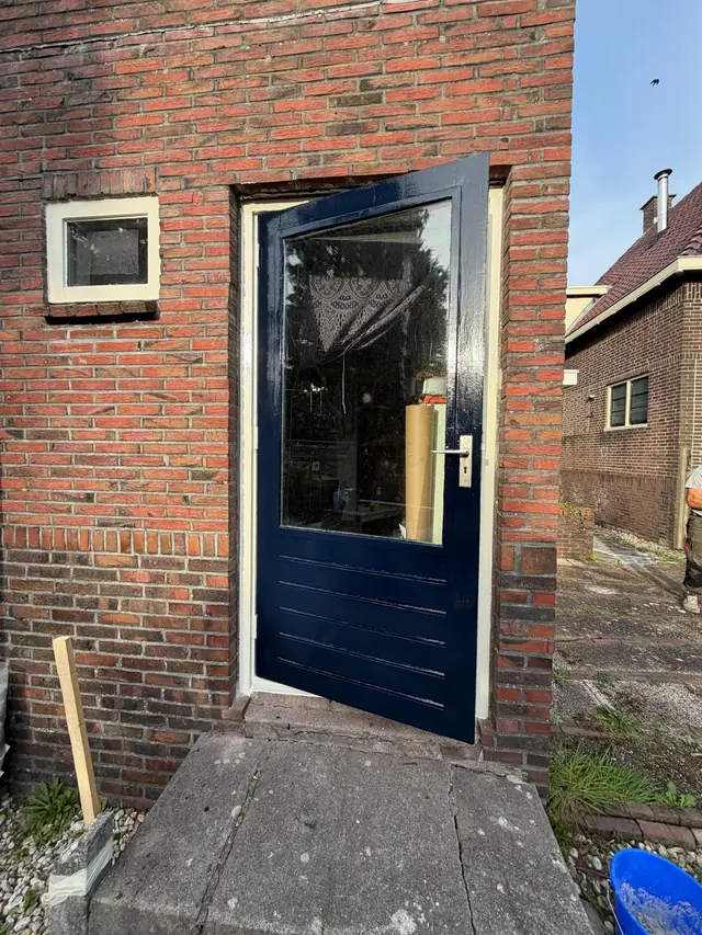 Donkerblauw geschilderde achterdeur met glas in een bakstenen gevel