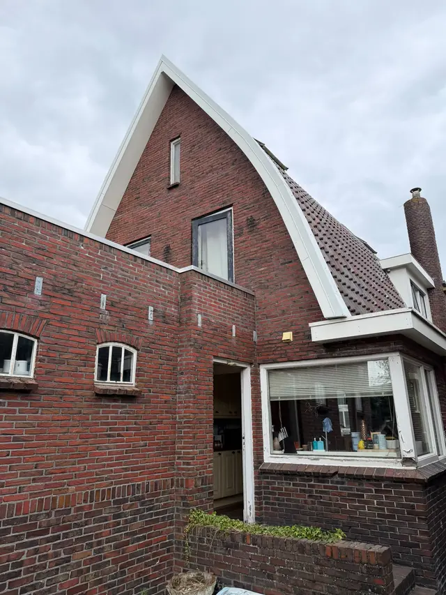 Bakstenen puntgevel en erker met nieuwe witte boeiboorden onder een bewolkte lucht