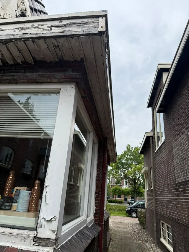 Erker met afgebladderd houtwerk en een aangetaste dakrand, vóór het herstel