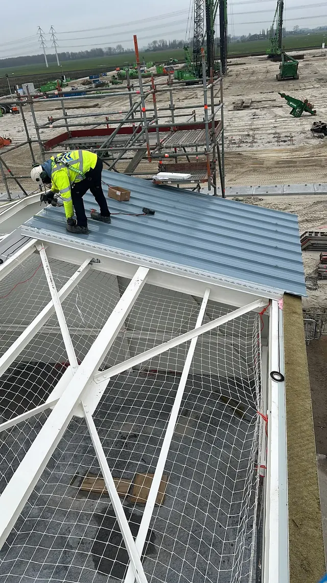 Vakman in veiligheidskleding op het dak van een stalen hal