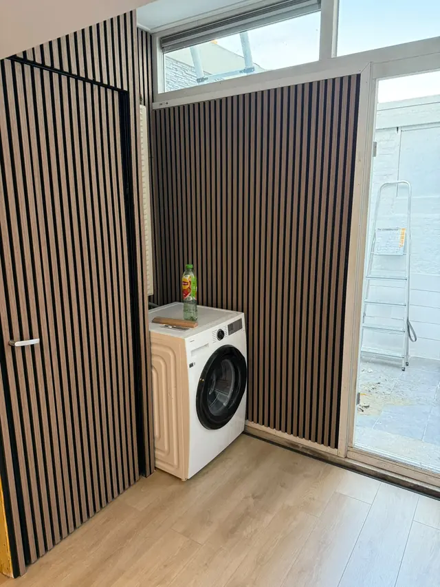 Gerenoveerde studio met wanden van houten lamellen, een verborgen deur en een lichte houten vloer