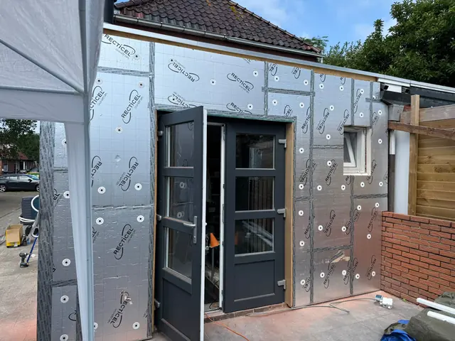 Uitbouw in aanbouw met isolatieplaten rond antraciete openslaande deuren