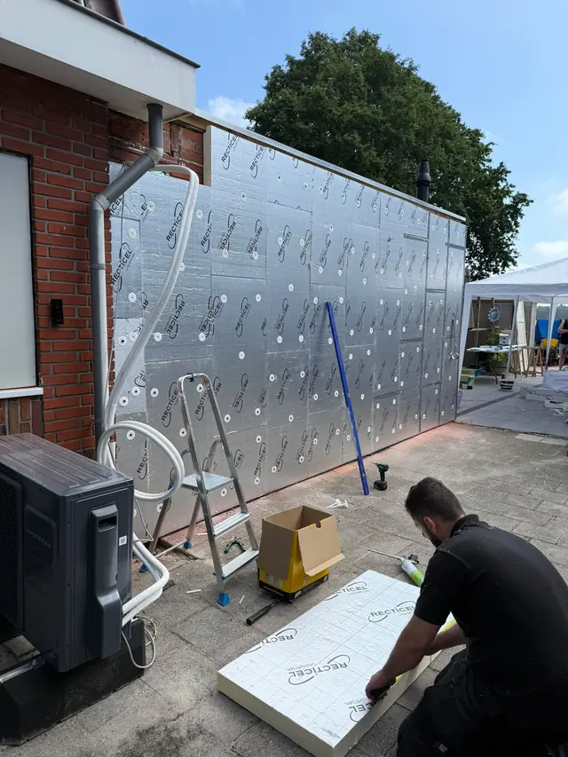Vakman snijdt een isolatieplaat op maat naast een uitbouw in aanbouw
