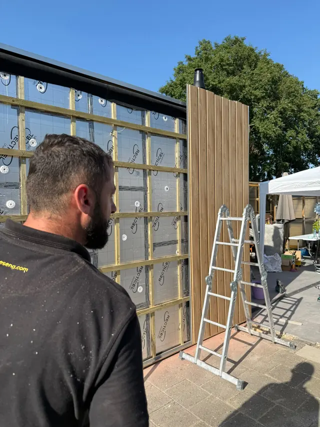Vakman bekijkt de geïsoleerde gevel van een uitbouw in aanbouw